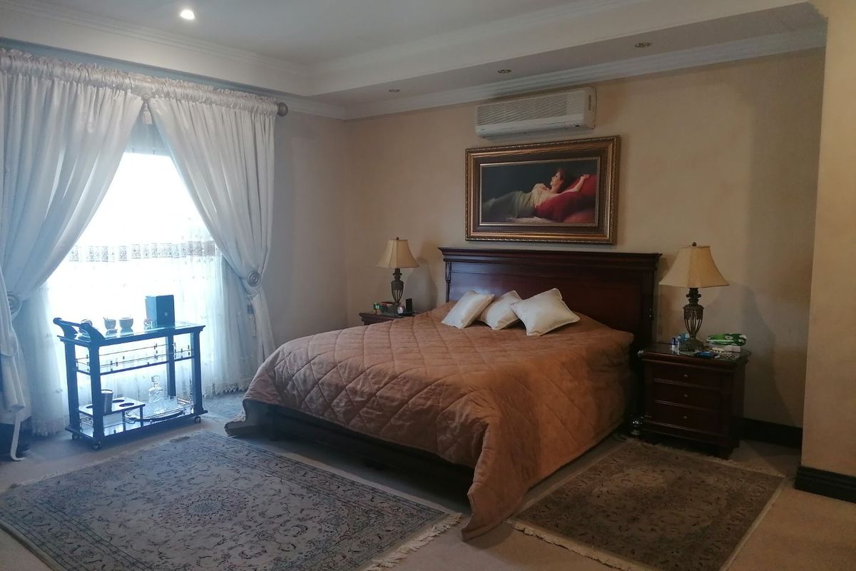 A spacious bedroom featuring recessed ceiling lighting, cove molding, and a wall-mounted air conditioning unit, finished with neutral carpeting.