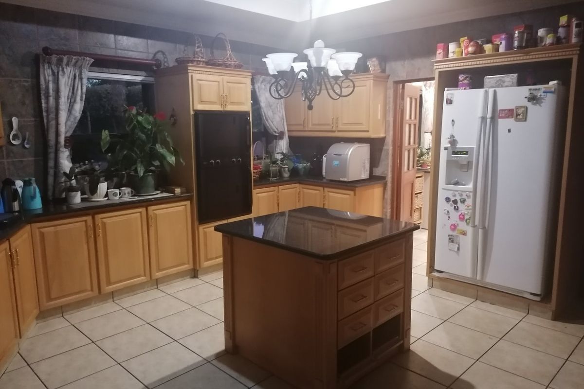 A spacious kitchen featuring light wood cabinetry, granite countertops, a central island, and tiled flooring, offering a functional layout with ample storage space.