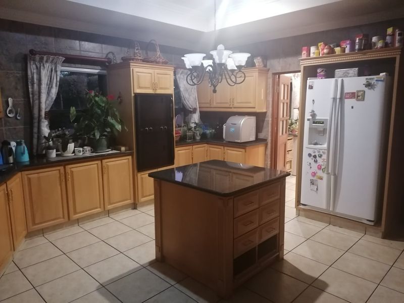 A spacious kitchen featuring light wood cabinetry, granite countertops, a central island, and tiled flooring, offering a functional layout with ample storage space.