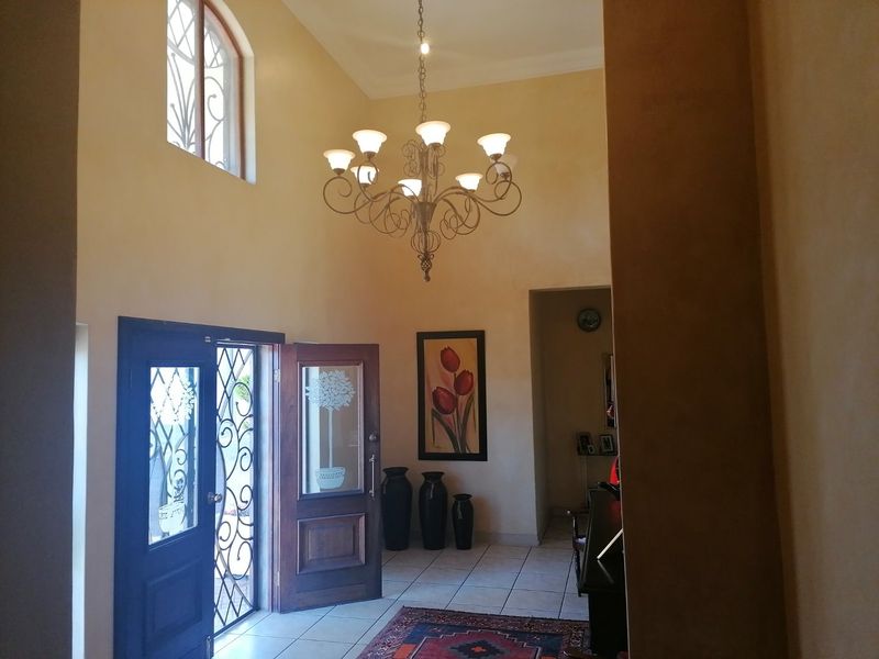 Spacious entrance hall featuring high ceilings, a decorative chandelier, tiled flooring, and a secure wrought iron front door with glass inserts.