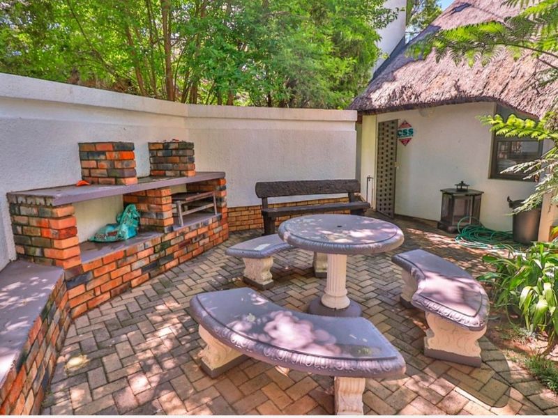 Outdoor patio area featuring a built-in brick braai, paved flooring, and a thatched roof structure, set within a private garden space.