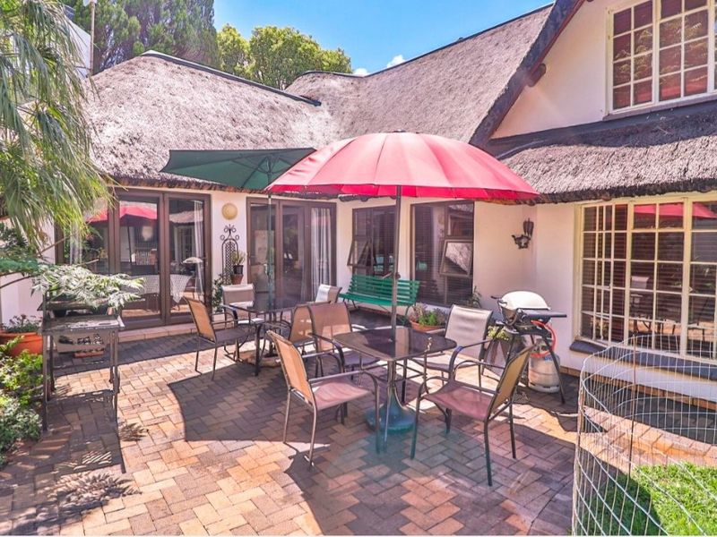 A paved outdoor patio area featuring a traditional thatched roof structure and multiple access points to the interior through sliding glass doors.