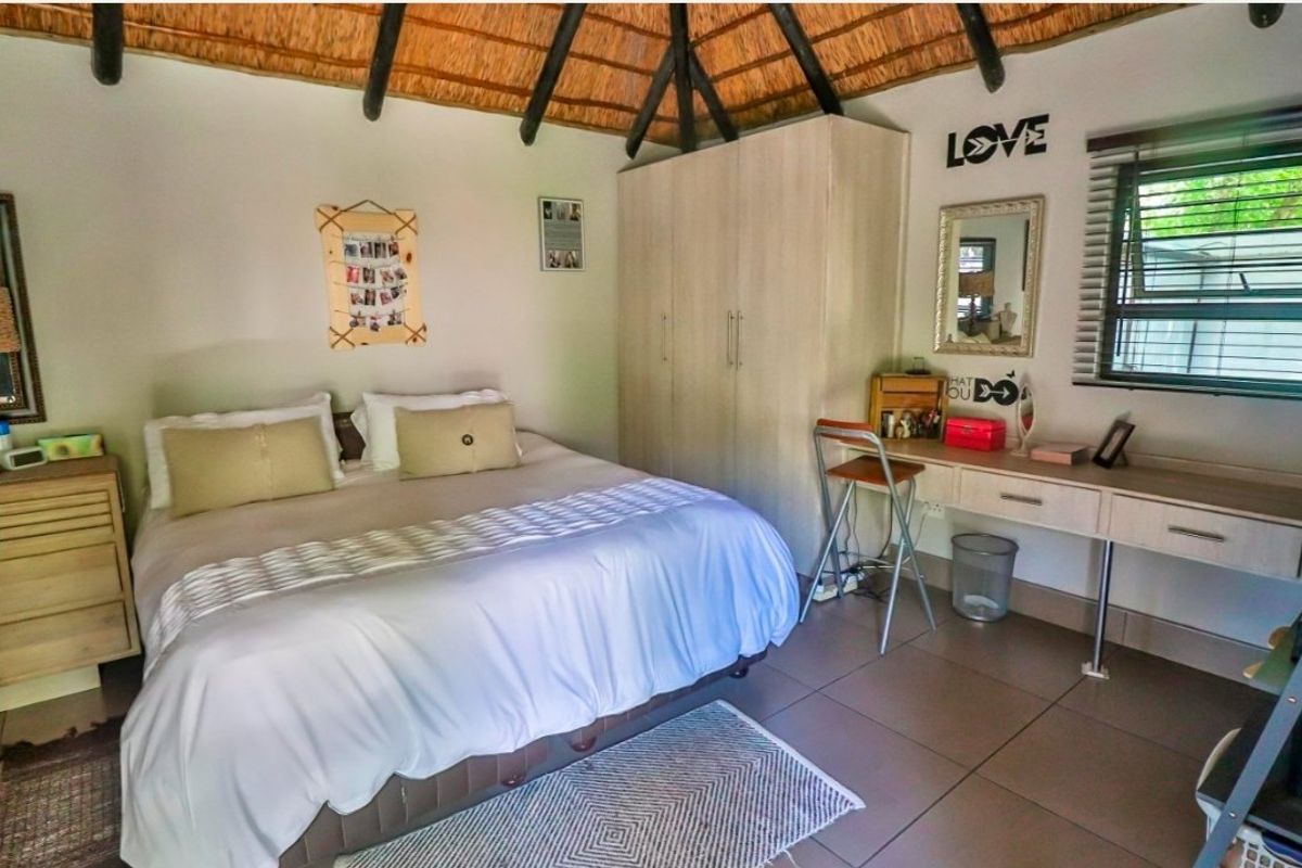 A bedroom featuring a unique thatched ceiling with exposed timber rafters, built-in wardrobe, integrated desk, and tiled flooring.