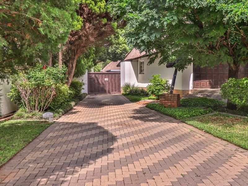 A paved driveway leading to a property entrance with a garage, surrounded by mature trees and a landscaped garden.