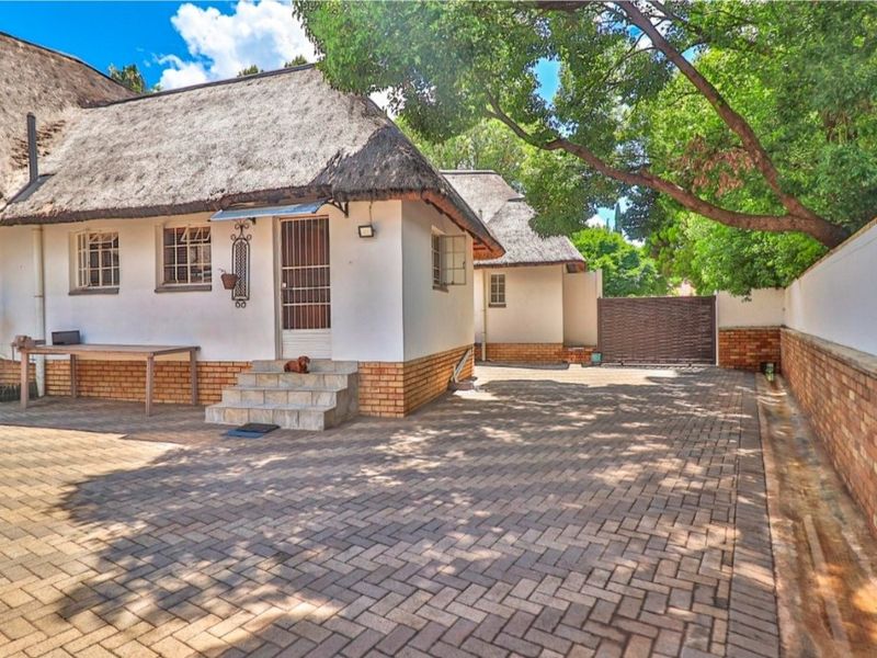 Front exterior view of a house featuring a traditional thatch roof, brick paved driveway, and secure perimeter walling.