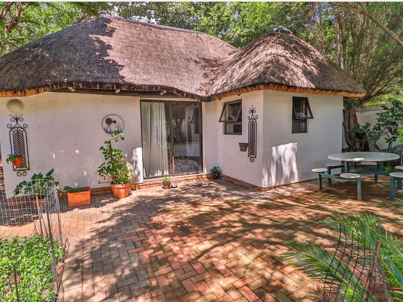 A charming rear exterior view featuring a traditional thatched roof, brick paved patio area, and sliding glass door access to the home.