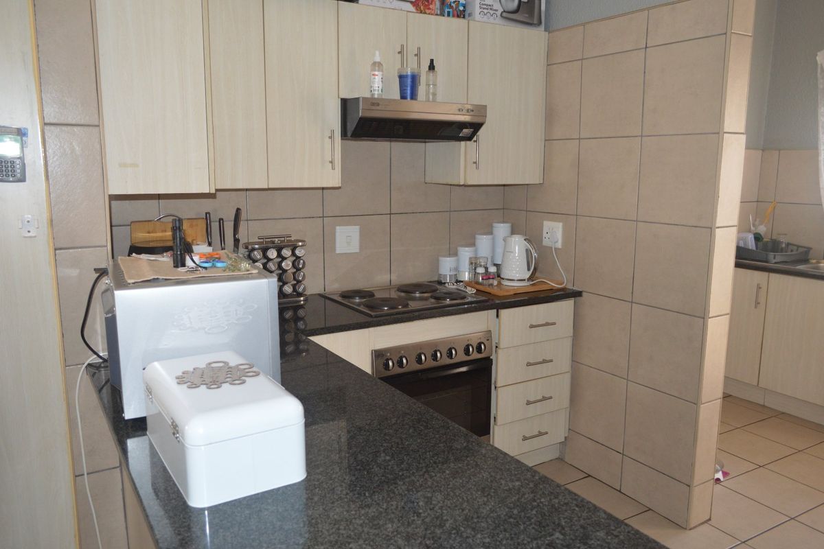 A functional kitchen featuring granite countertops, built-in oven with electric hob, extractor fan, and tiled splashback with ample cabinetry.