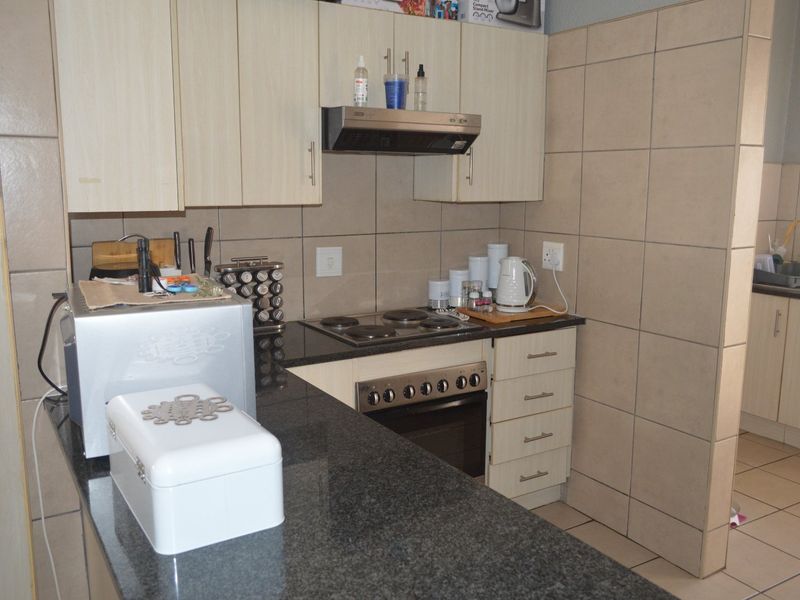 A functional kitchen featuring granite countertops, built-in oven with electric hob, extractor fan, and tiled splashback with ample cabinetry.
