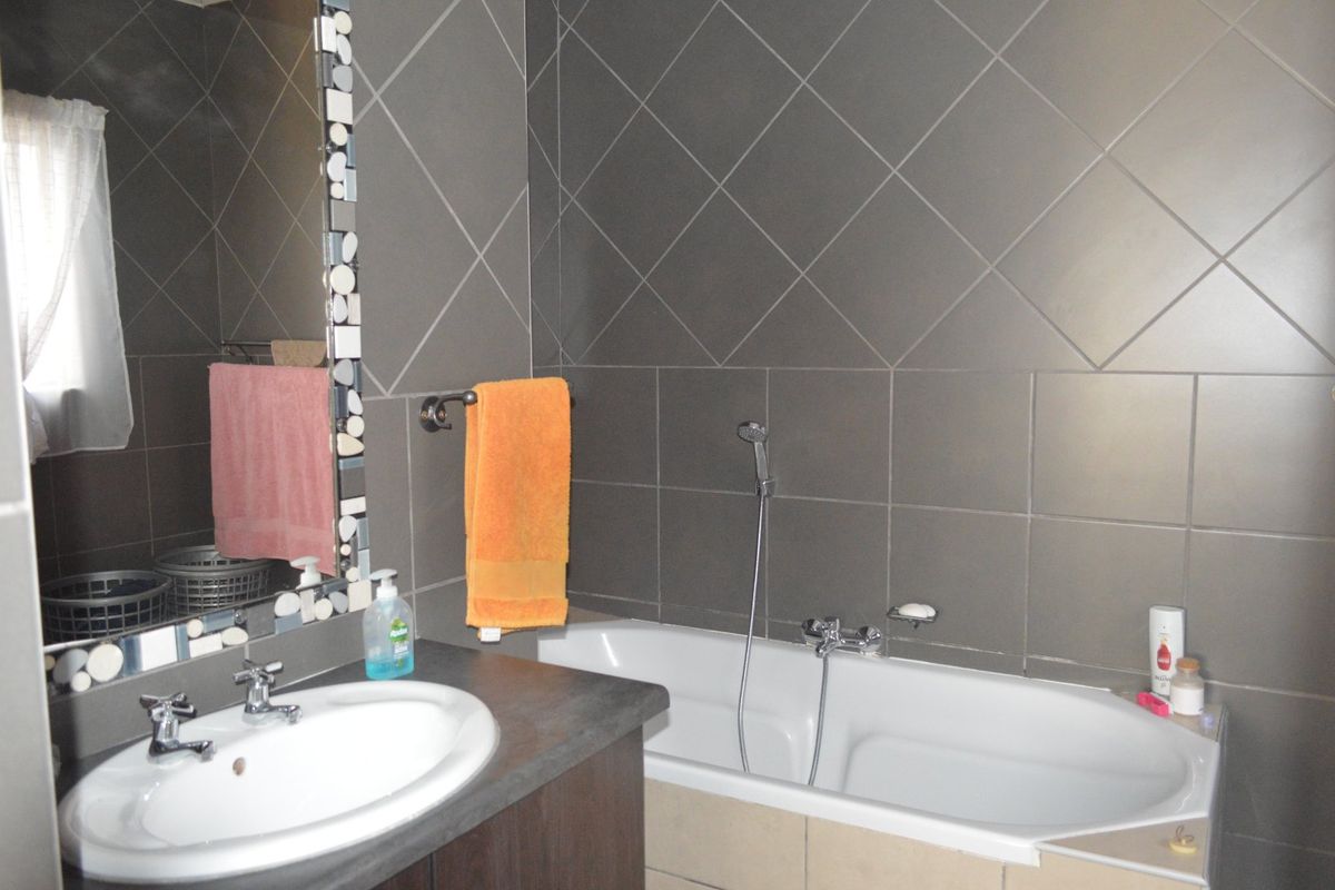 A functional bathroom featuring a built-in vanity with a drop-in basin, a bathtub with a handheld shower mixer, and dark tiled wall finishes.
