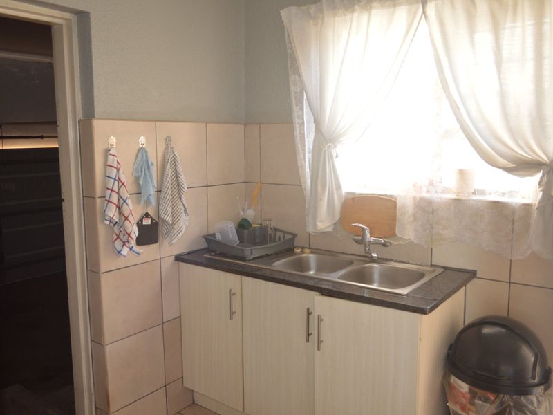 A functional scullery area featuring a double stainless steel sink, tiled splashback, and built-in laminate cabinetry, providing practical utility space.