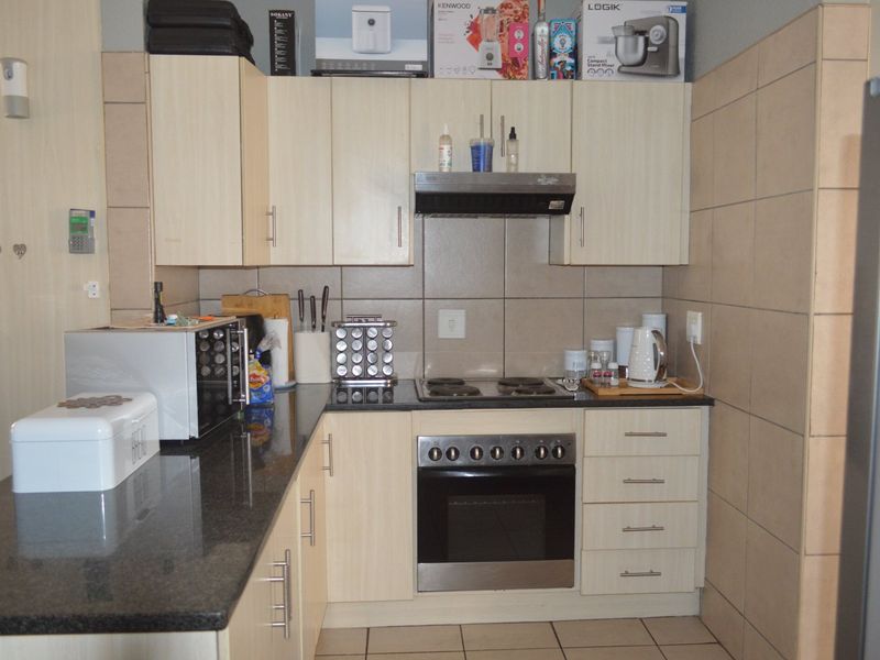 A functional kitchen featuring light wood cabinetry, granite countertops, a built-in oven with hob, and tiled splashbacks.
