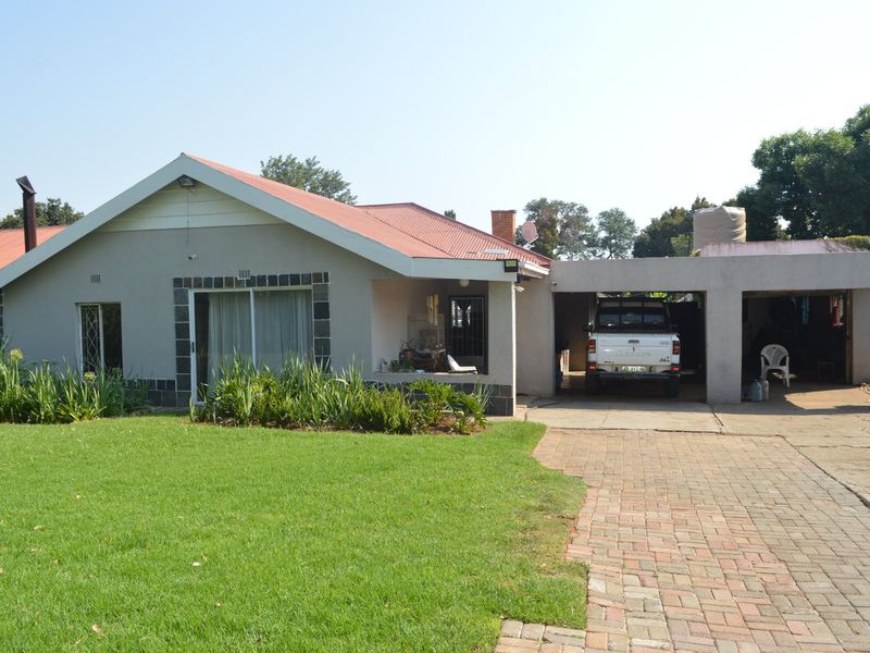 Front view of a single-story house featuring a corrugated metal roof, a brick-paved driveway, and an attached double carport with a well-maintained front lawn.
