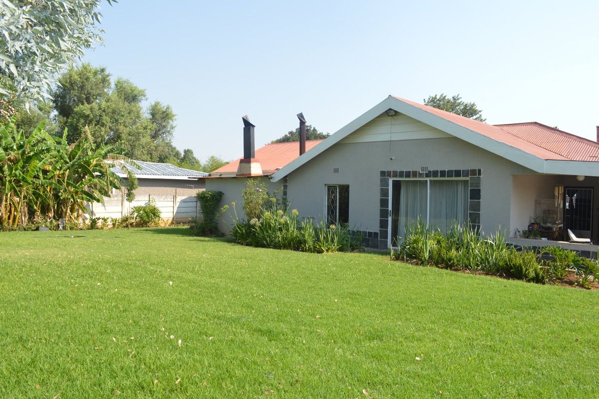 Rear view of the house featuring a spacious lawn, metal roofing, and an external chimney stack with sliding door access to the interior.