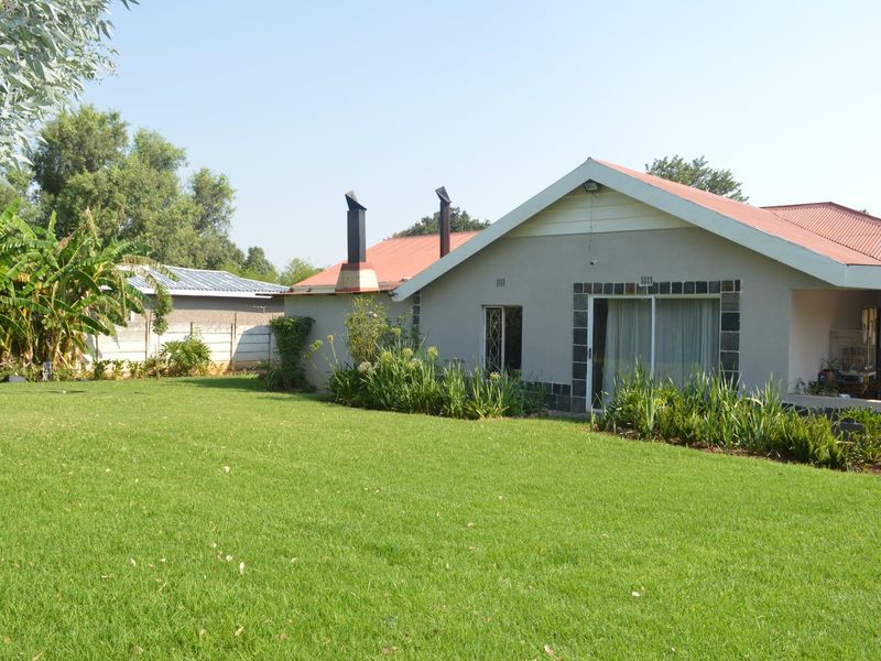 Rear view of the house featuring a spacious lawn, metal roofing, and an external chimney stack with sliding door access to the interior.