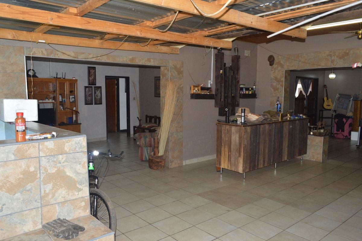Spacious living area featuring tiled floors, stone-clad pillars, and an exposed timber beam ceiling with a built-in bar counter.