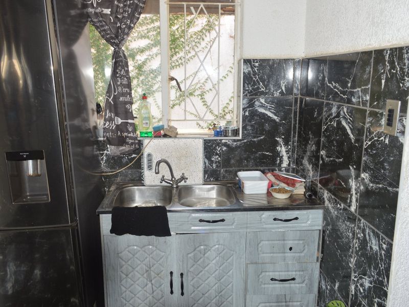 Compact scullery area featuring a double basin stainless steel sink, built-in cabinetry, and dark marble-effect wall tiling.