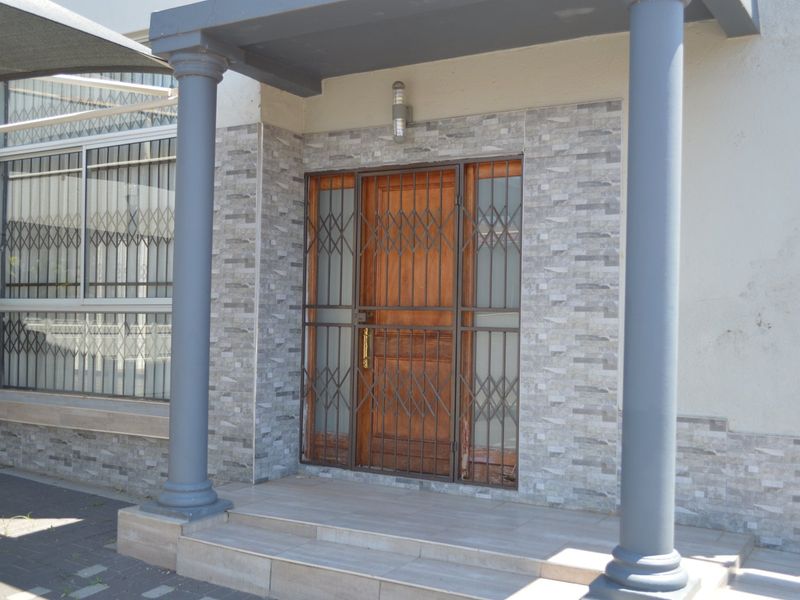 Front entrance featuring a wooden door with security gate, stone-clad facade, tiled porch area, and structural columns.