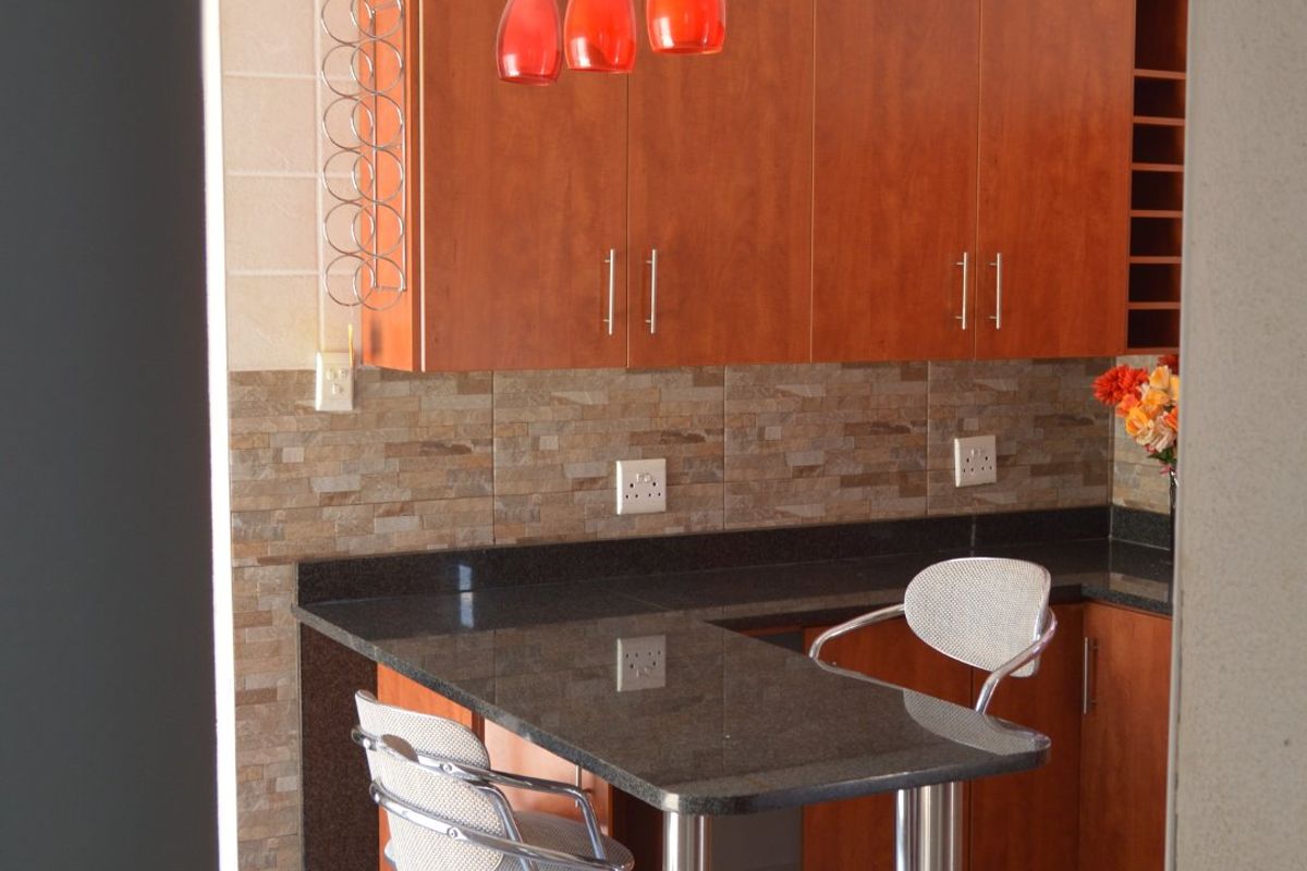 A functional kitchen featuring warm-toned wooden cabinetry, granite countertops, a stone tile backsplash, and a convenient breakfast bar with pendant lighting.