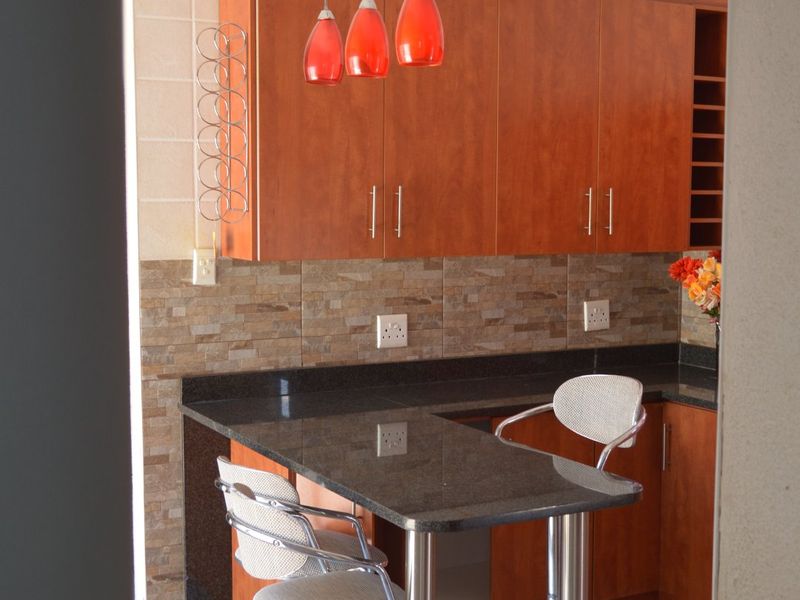 A functional kitchen featuring warm-toned wooden cabinetry, granite countertops, a stone tile backsplash, and a convenient breakfast bar with pendant lighting.