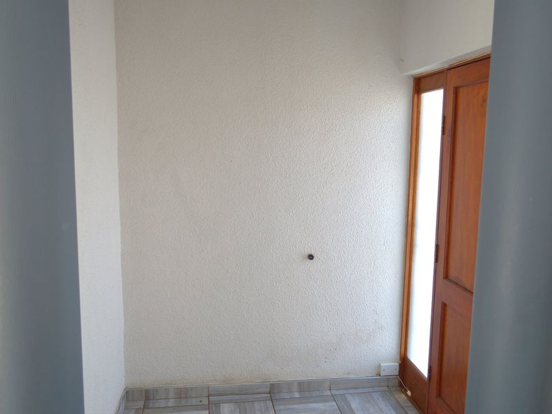 A simple, empty entryway featuring tiled flooring and a wooden door with glass paneling.