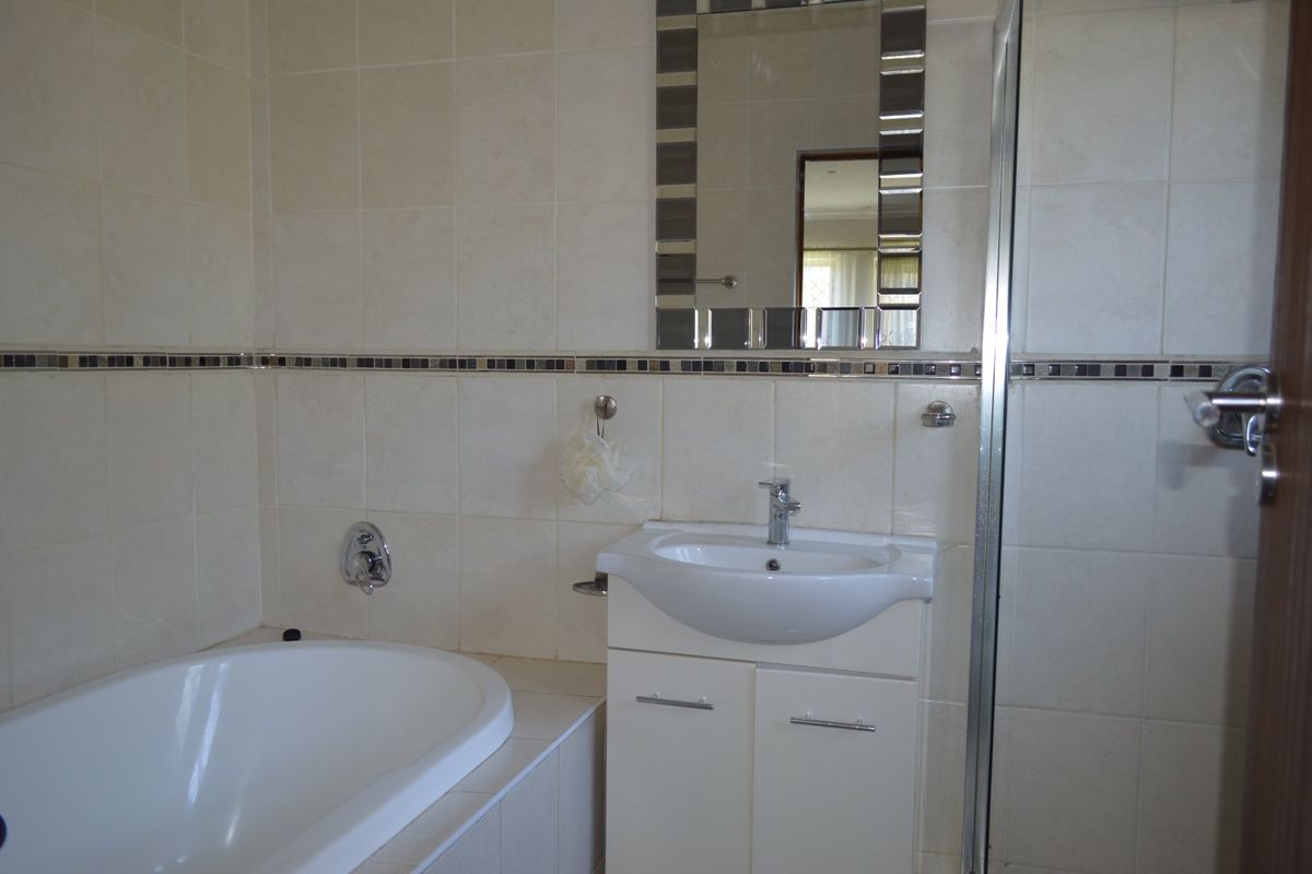 A clean, functional bathroom featuring a built-in vanity, ceramic basin, bathtub, and a separate shower enclosure with neutral wall tiling.