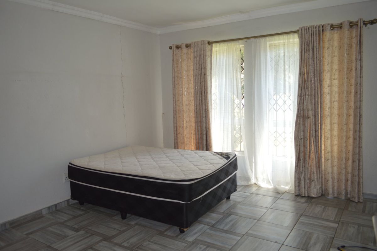 A bedroom featuring tiled flooring and a security gate on the window, currently vacant with a visible wall crack requiring attention.