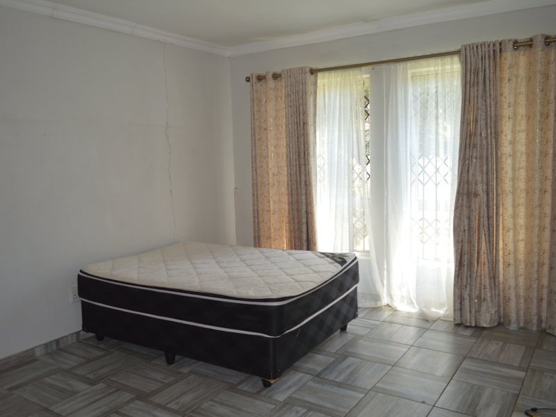 A bedroom featuring tiled flooring and a security gate on the window, currently vacant with a visible wall crack requiring attention.