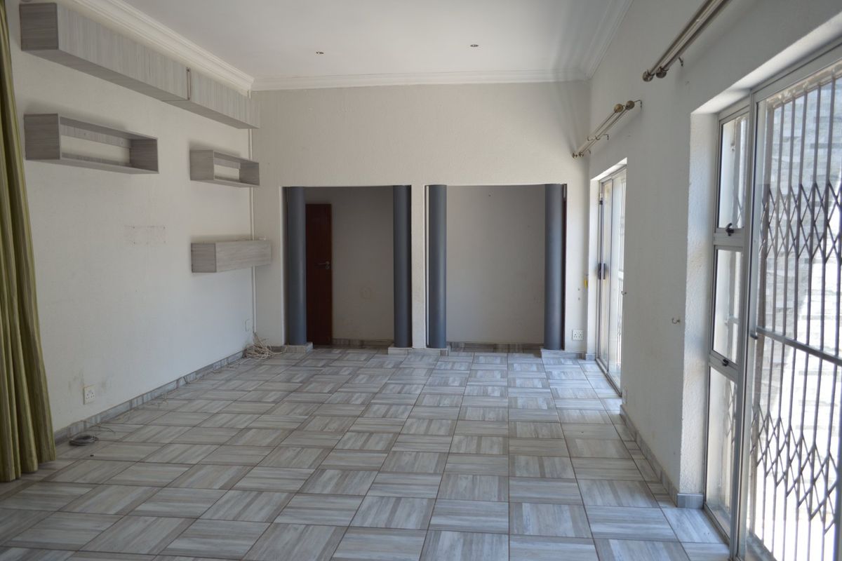An empty living room featuring tiled flooring, built-in wall shelving, structural columns, and sliding glass doors leading to an outdoor area.