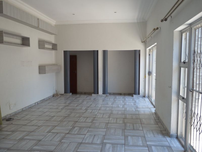 An empty living room featuring tiled flooring, built-in wall shelving, structural columns, and sliding glass doors leading to an outdoor area.