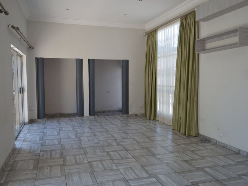 An empty, open-plan living area featuring tiled flooring, decorative columns, and large windows with curtains, offering a blank canvas for interior design.