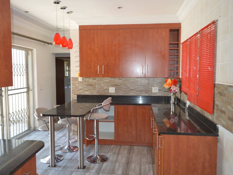 A functional kitchen featuring warm-toned cabinetry, granite countertops, stone tile backsplash, and a breakfast bar area with direct access to the exterior.