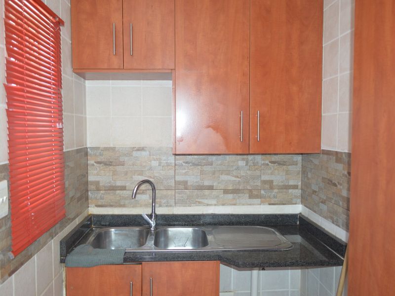 A functional scullery area featuring laminated cabinetry, granite countertops, a double bowl stainless steel sink, and a tiled splashback.