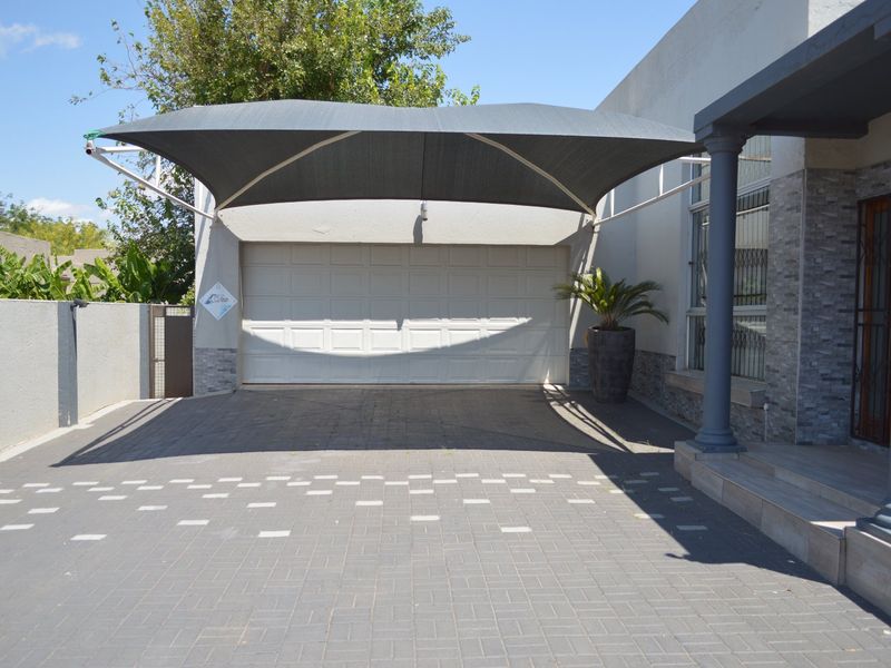 Front exterior view featuring a paved driveway, a modern shade sail covering the garage area, and stone-clad architectural details at the entrance.