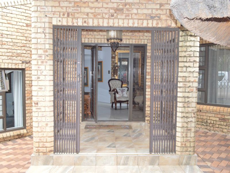 Entrance area featuring a face brick facade, secure metal gate, and tiled patio leading into the home interior.