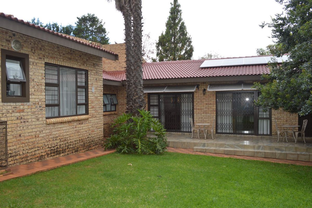 Rear view of a face brick house featuring a tiled patio, solar panels, and a well-maintained garden area.