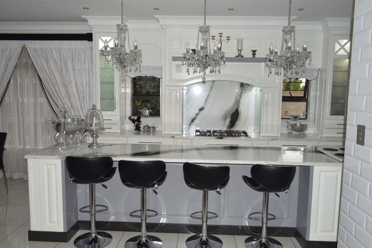 A high-end kitchen featuring a large marble island, integrated gas cooktop, custom cabinetry, and elegant marble splashback with sophisticated lighting.