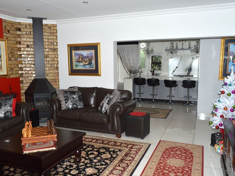 Spacious open-plan living area featuring a prominent brick fireplace and a seamless transition to a modern kitchen with a breakfast bar island.