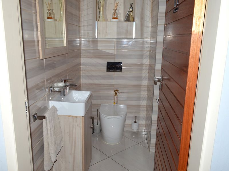 A compact, modern bathroom featuring tiled walls and flooring, a wall-mounted toilet, and a vanity unit with a basin.