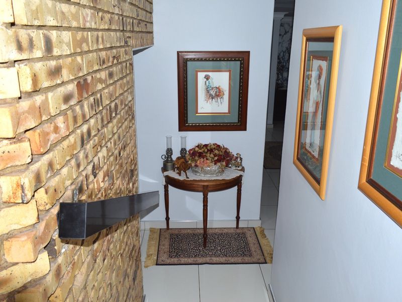 A hallway featuring an exposed brick wall, tiled flooring, and a handrail, leading into the interior of the home.
