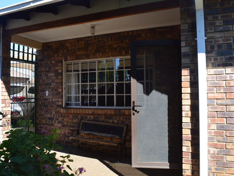 A covered patio area featuring face brick walls, paved flooring, and a secure entrance door with a security gate.