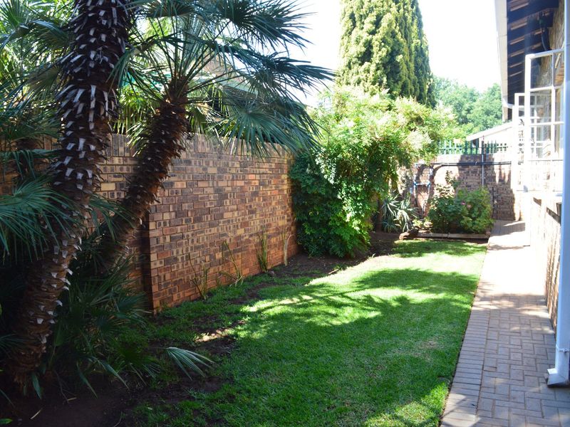 A private rear garden area featuring a well-maintained lawn, paved walkway, and established brick boundary walls.