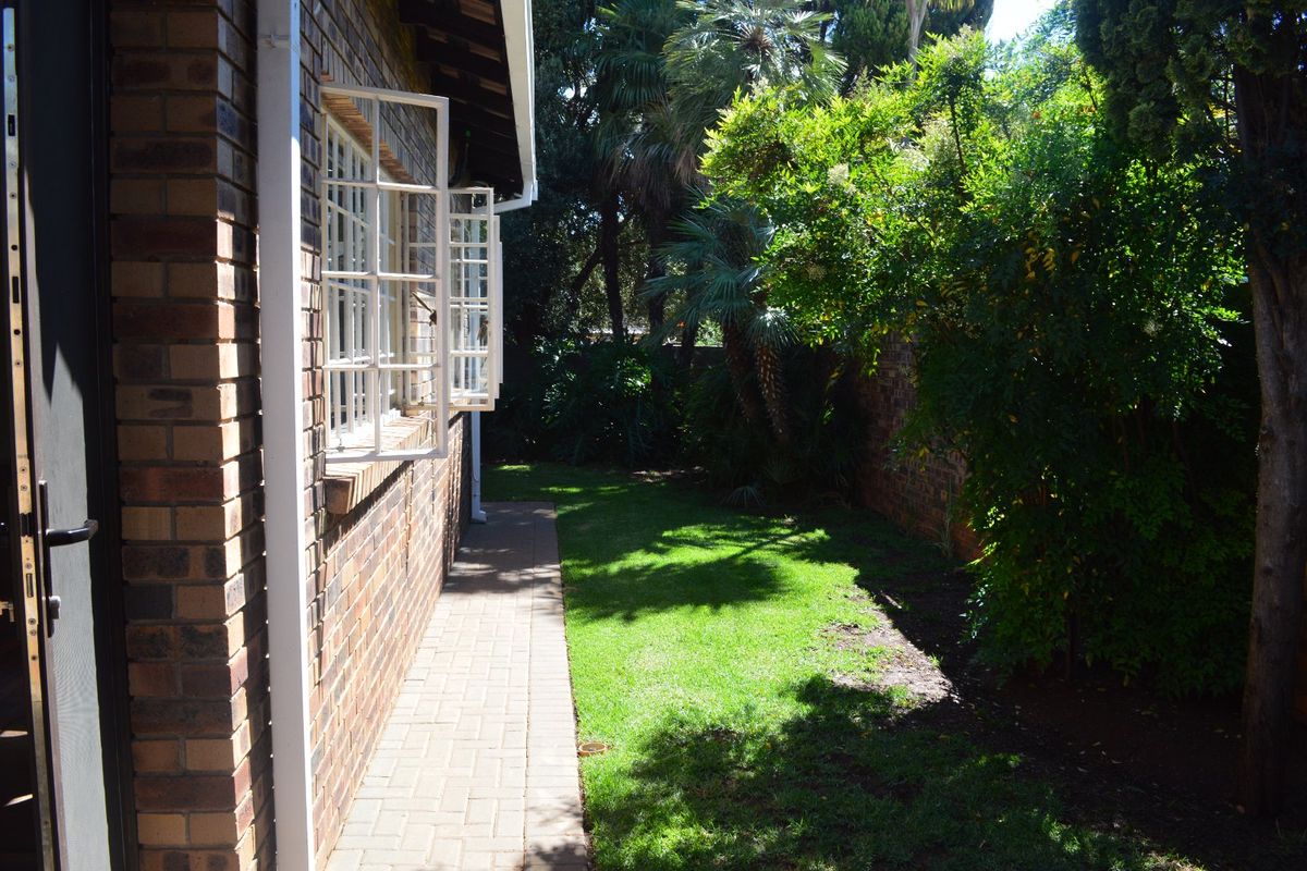 A view of the rear garden featuring a paved walkway alongside the face brick exterior wall and established greenery.