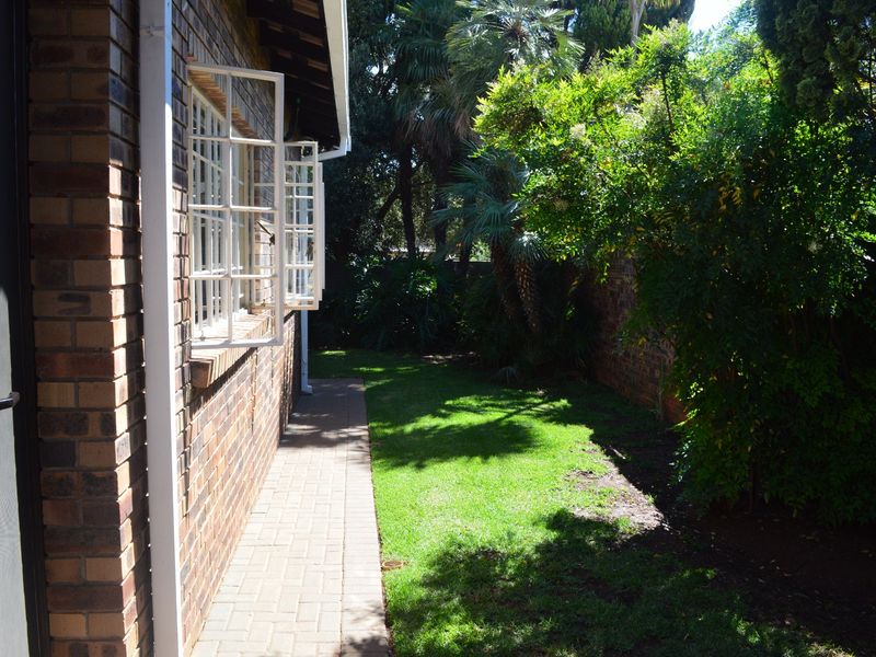 A view of the rear garden featuring a paved walkway alongside the face brick exterior wall and established greenery.