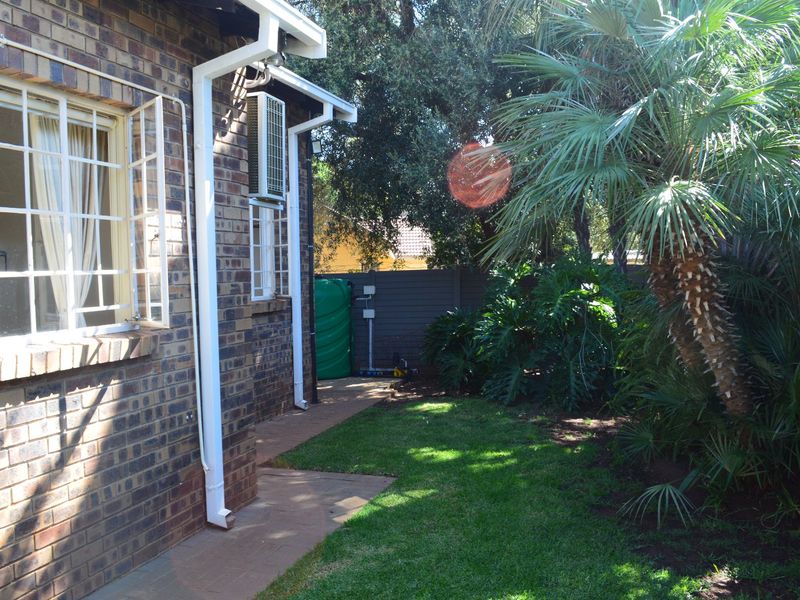 A private rear garden area featuring a face brick townhouse exterior, paved pathway, established landscaping, and a water storage tank.