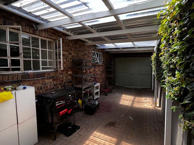 A covered outdoor patio area featuring brick paving, exposed brick walls, and a translucent corrugated roof, providing a functional transition space.