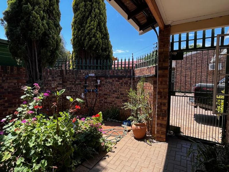 A private, paved patio area featuring a brick boundary wall, secure metal gate, and covered roof structure, providing a pleasant outdoor space.