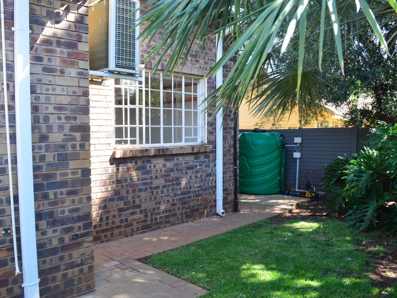 Rear exterior view of the townhouse featuring face brick walls, a paved walkway, security window bars, and a water storage tank.
