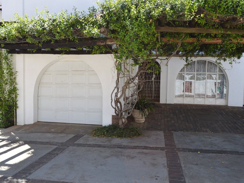 Front exterior view of the townhouse featuring a garage, paved driveway, and a shaded pergola entrance with mature climbing vines.