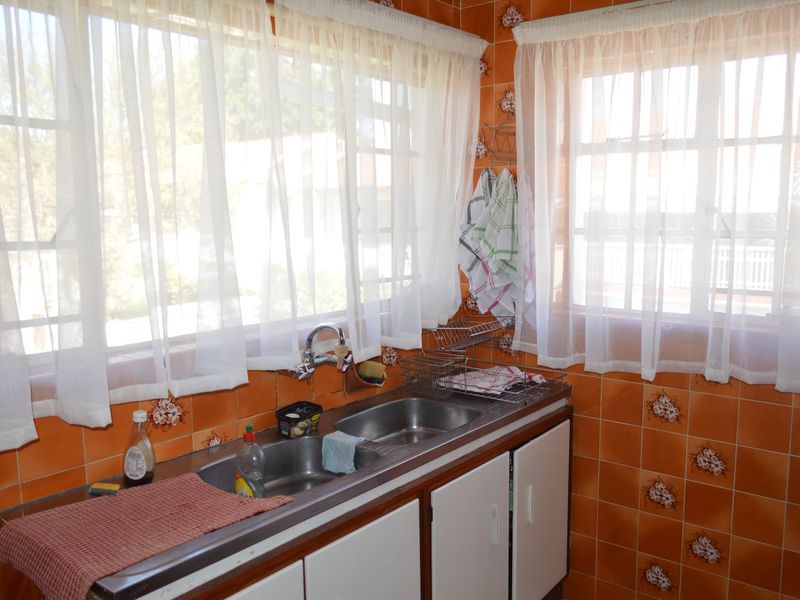 A dated kitchen area featuring a double stainless steel sink, built-in cabinetry, and orange patterned wall tiles.