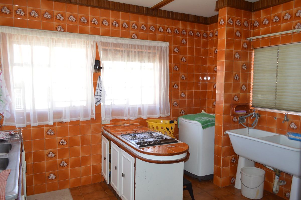 A dated kitchen featuring orange decorative wall tiles, built-in cabinetry, a gas hob, and a traditional ceramic sink.